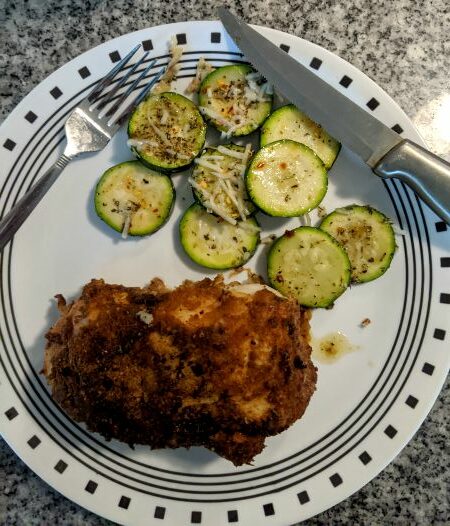 Chicken Kiev and sliced, baked zucchini topped with shredded cheese on white plate with knife and fork