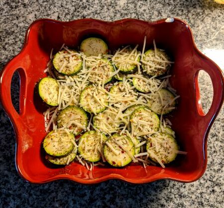 Sliced zucchini topped with shredded cheese in a red ceramic bowl.