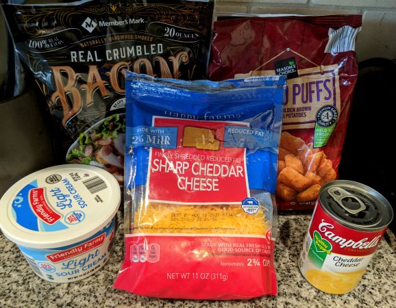 Ingredients on countertop- sour cream, sharp shredded cheddar cheese, cheddar cheese condensed soup, crumbled bacon, and frozen tater tots.