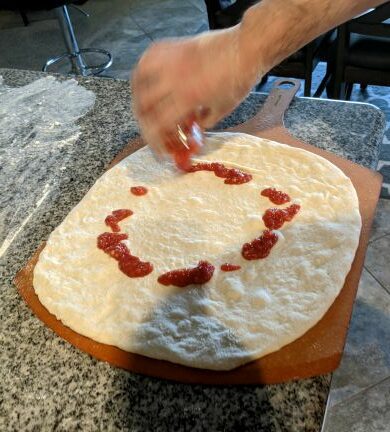 Man adding sauce to a pizza dough