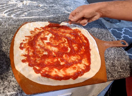 Man adding sauce to a pizza dough