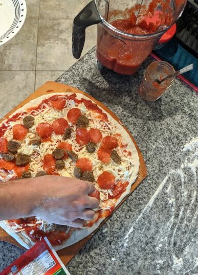 Sausage and pepperoni toppings being added to pizza