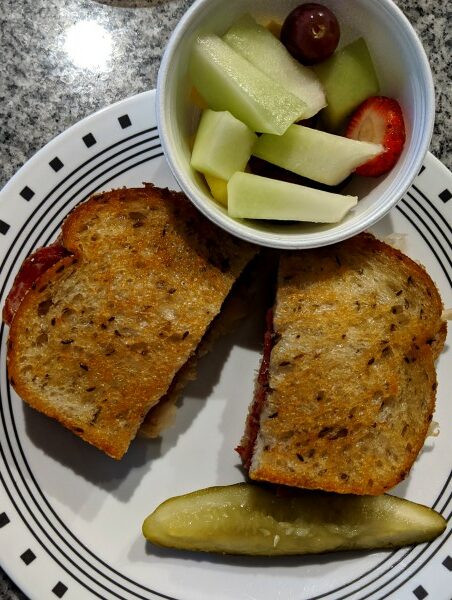 Sandwich with Pickle and Cup of Fruit on Plate
