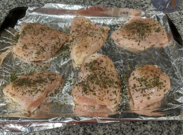 Chicken on pan before baking, seasoned with salt, pepper, and cilantro