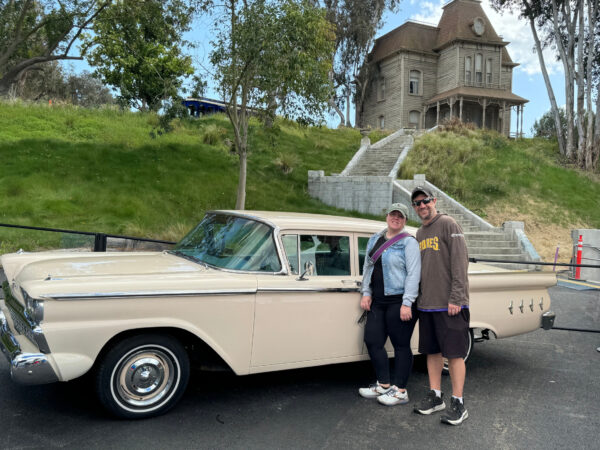 Couple posing with Norman Bates Car outside of the Bates Motel (unseen) and Mother's house from Psycho for the Universal Studios Hollywood Studio Tour Special Edition for Universal Studios 60th Anniversary